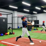 Hitclub baseball training scene with young athlete practicing swing in bright indoor facility.